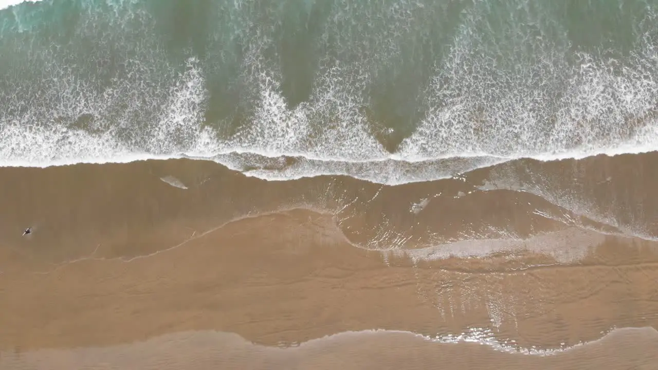 View from the sky down on the ocean waves and sandy beach on a warm summer day filmed from great height in 4k