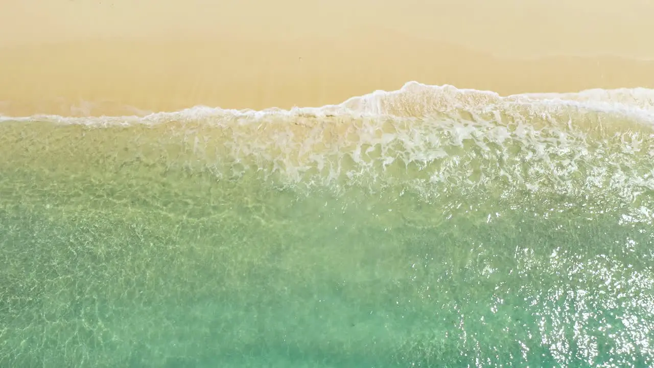 Aerial view of clear turquoise waves on sandy beach at tropical island in Indonesia