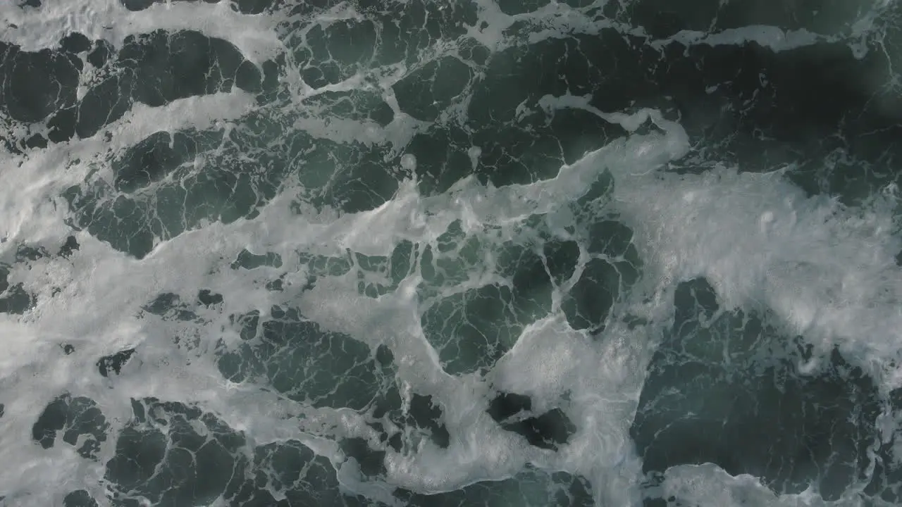 A top-down drone shot of white froth and waves rolling by in the sun