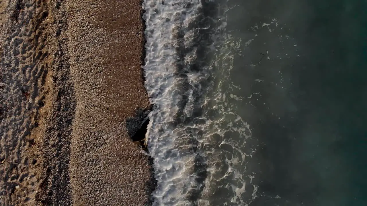 Sea waves splashing on big cliff covered by pebbles on remote beach of Mediterranean coastline