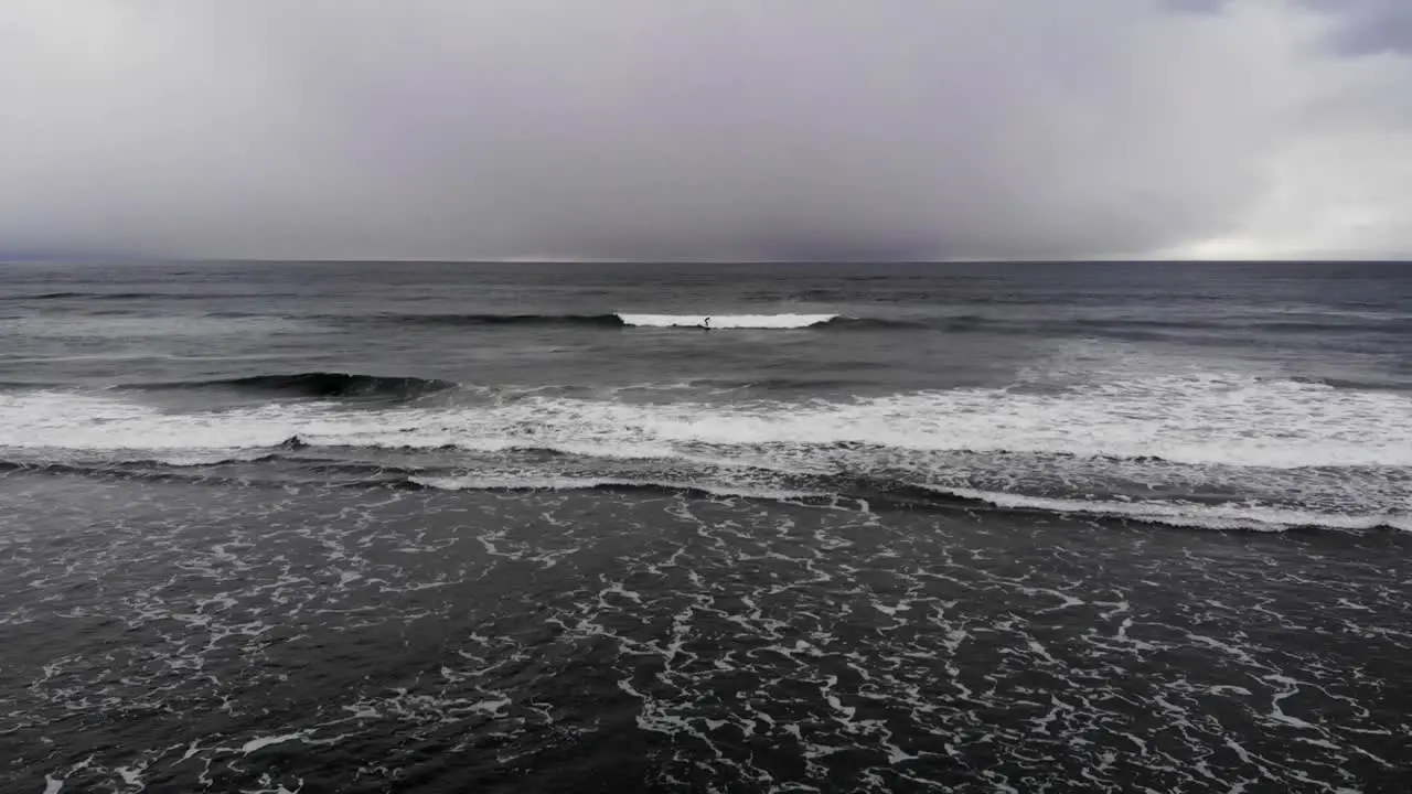 Drone flying out towards man catching a wave and surfing in