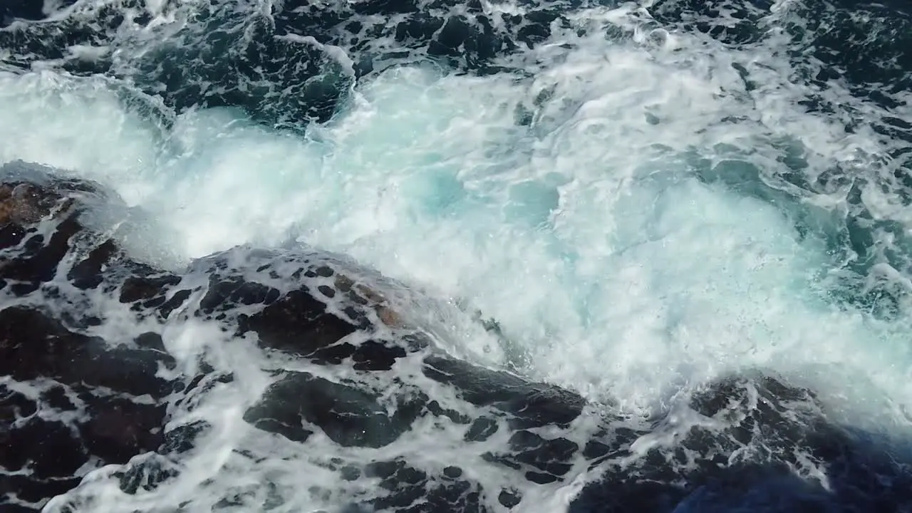 HD Hawaii Kauai slow motion static looking down at ocean waves crashing and swirling on rocks in lower left frame