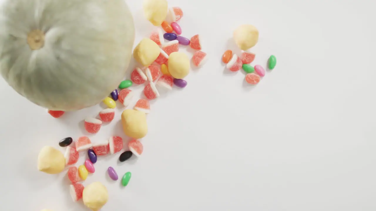 Overhead view of pumpkin and candies fallen against grey background