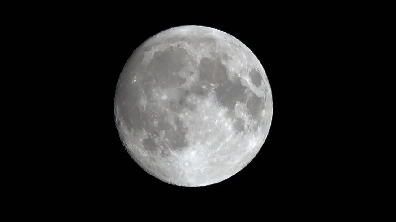 A bat flies across the face of a full moon slightly distorted by atmospheric turbulence