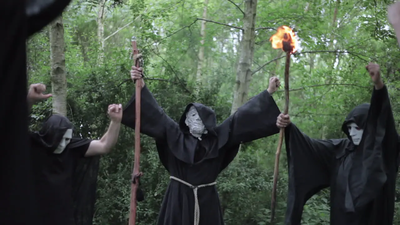 A cult meets in the woods to perform a ritual chant and the grand master raises his hands with a magical staff