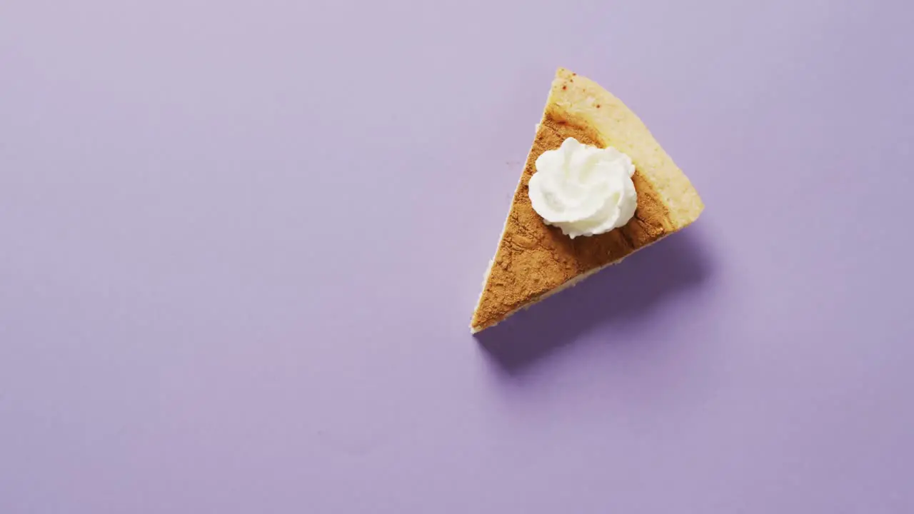 Video of piece of pumpkin pie with whipped cream on purple background