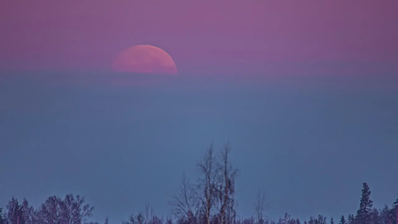 Time lapse of pink moon descending and disappearing behind clouds of colorful sky