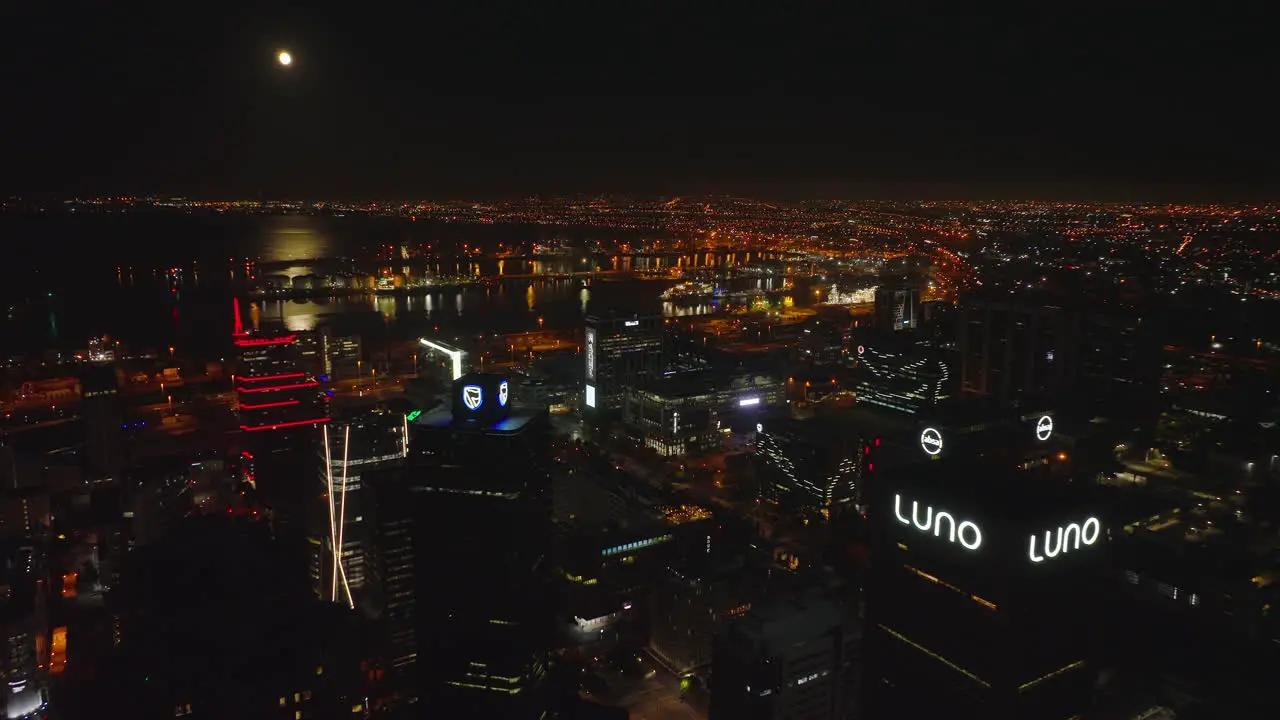 Elevated view of sea bay with harbour at night Backwards reveal of high rise office buildings in city centre Moonshine reflection on water surface Cape Town South Africa