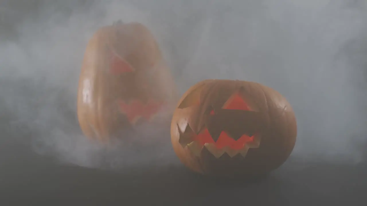 Smoke effect over two scary face carved halloween pumpkin against grey background