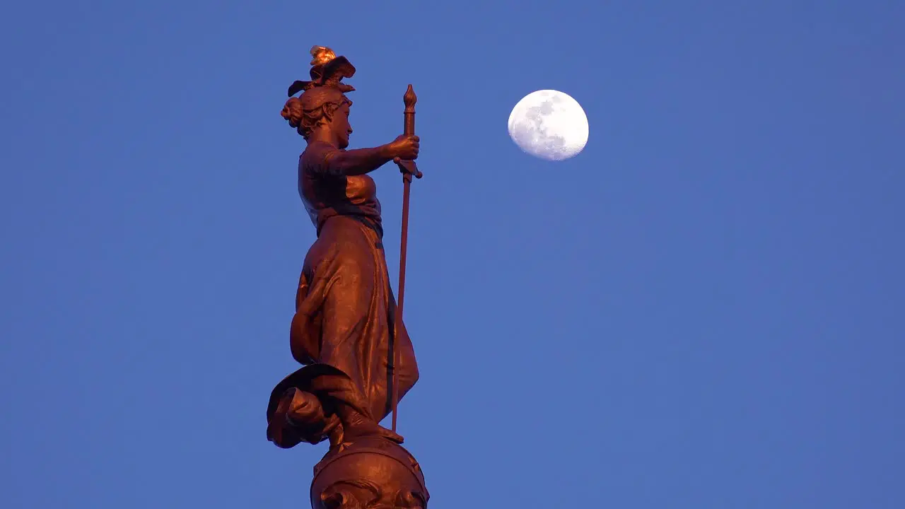 Statue atop Soldiers and Sailors Monument with moon rising in downtown Indianapolis Indiana