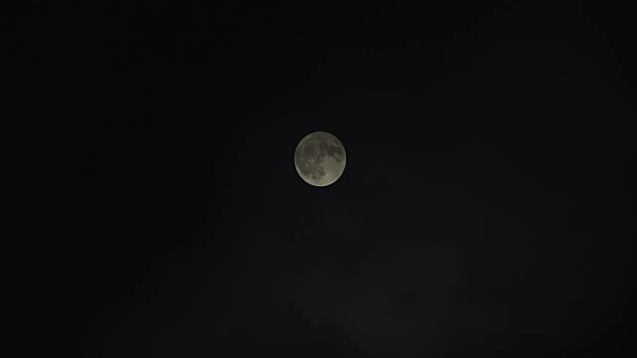 Wide shot of a full moon as fog passes by revealing full moon at the end