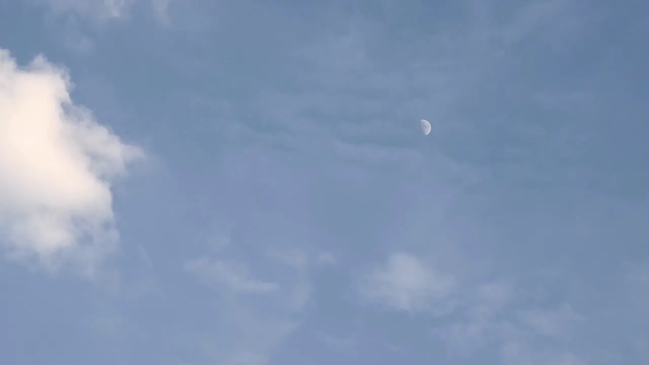 Moon in its first quarter time lapse as seen before dark with clouds almost covering it on the right side of the frame