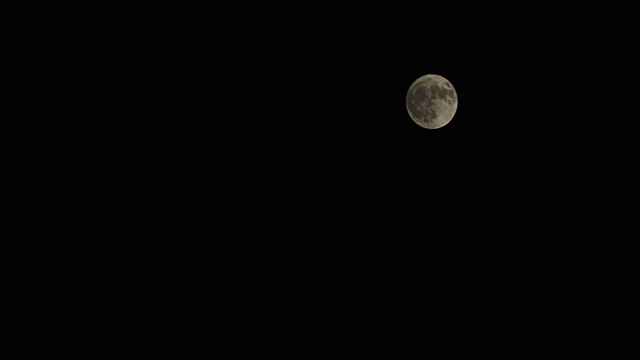 Time-lapse wide shot of a full moon with passing fog as it rises from the lower left to the upper right