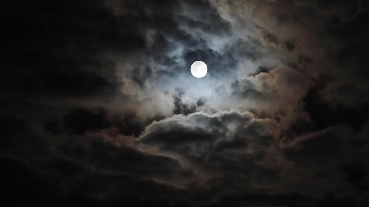 Timelapse of static full moon behind fast swirling clouds copy space