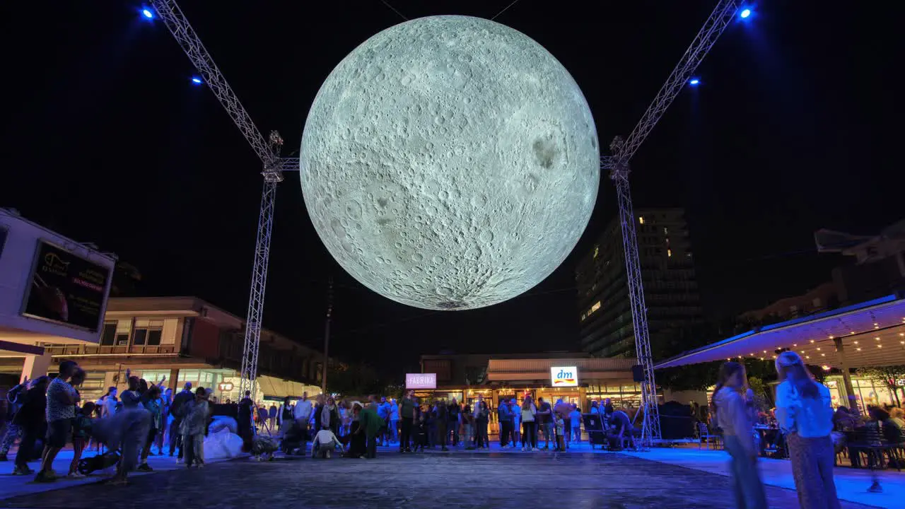 Large bright moon art exhibit at city square at night people taking selfies with supermoon timelapse