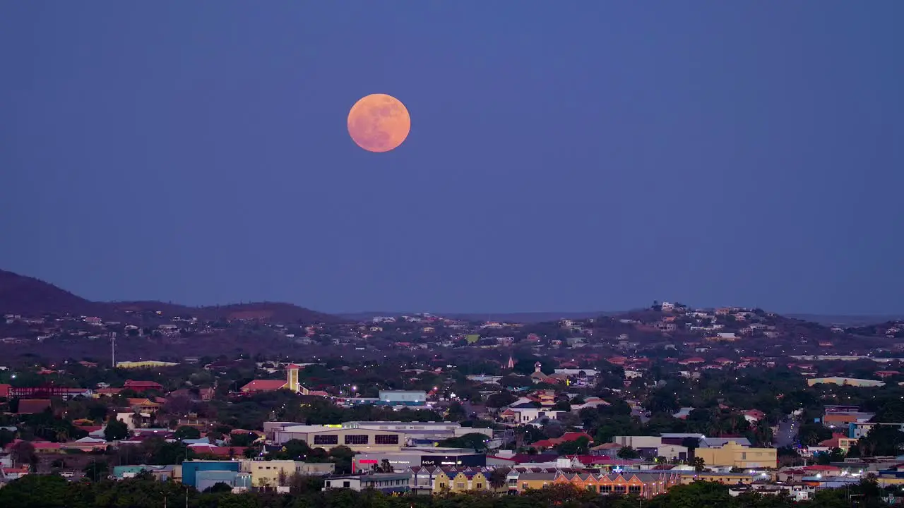 Large full blue supermoon glows red pan right to left above willemstad curacao