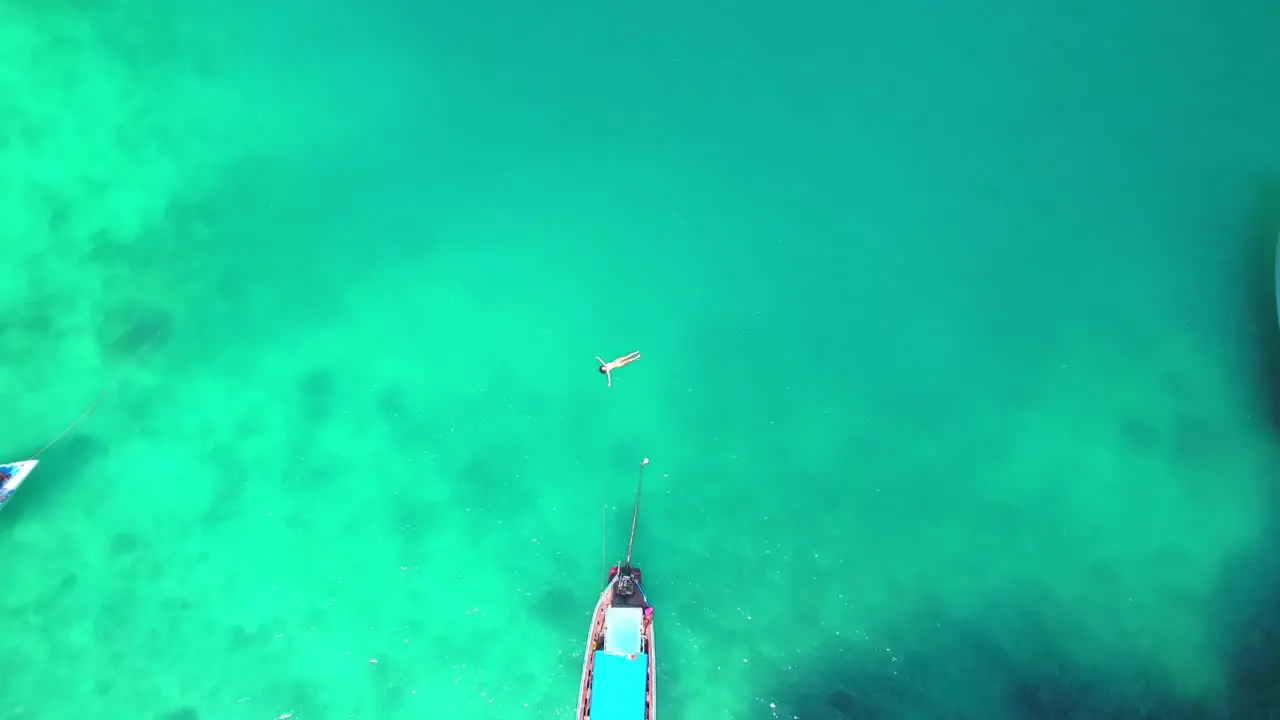 Aerial view of the girl that floats in turquoise water close to the boats