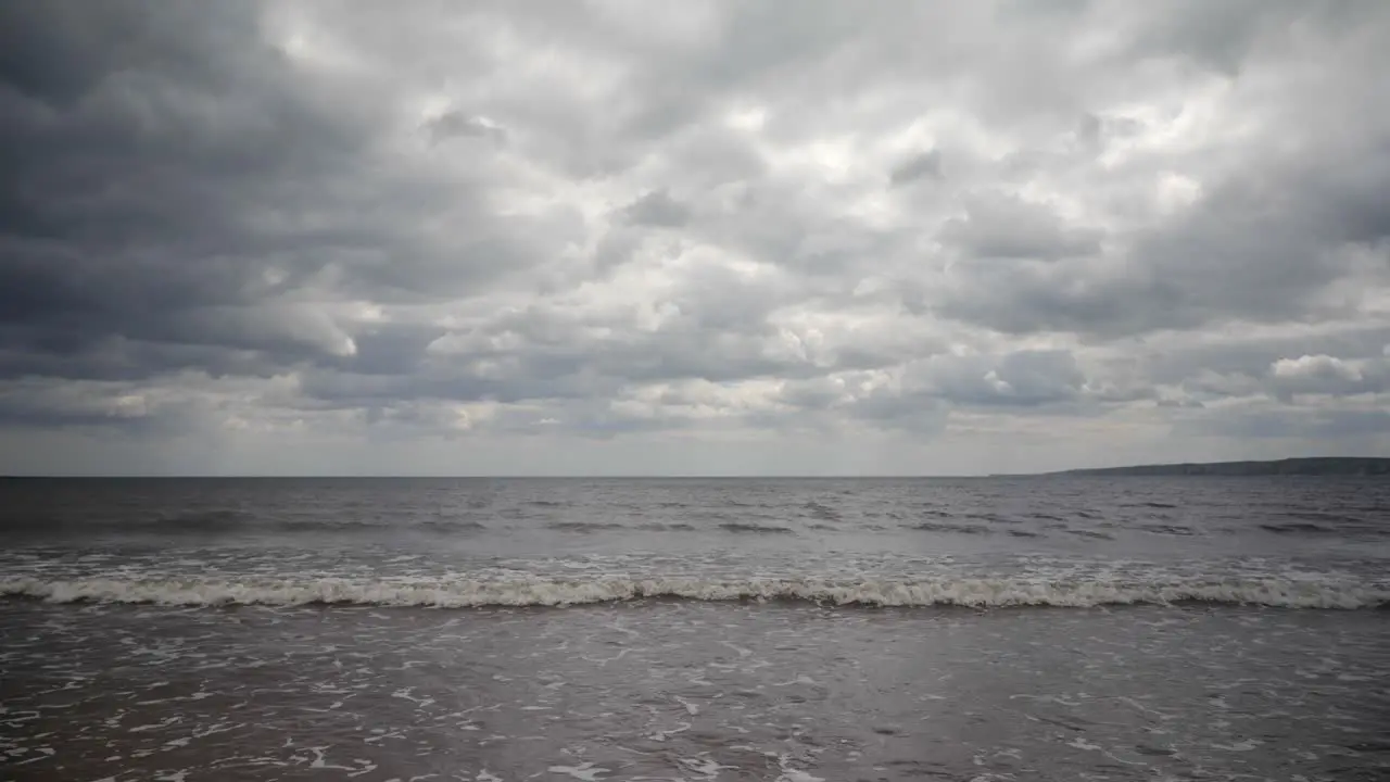 A view from the beach as waves lap at the shore with a dramatic overcast skyline