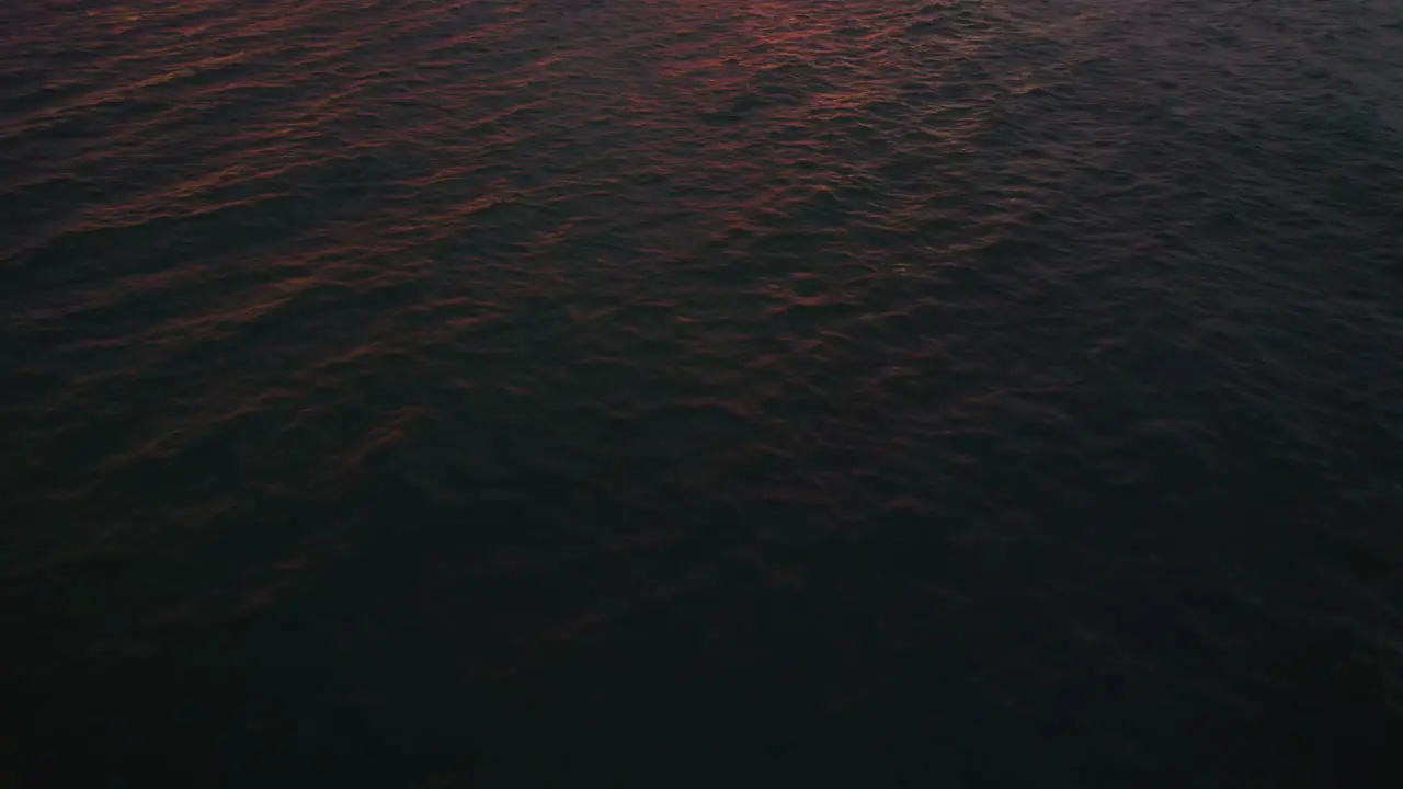 Flyover view of Pacific ocean waves tilting towards red sunset skies