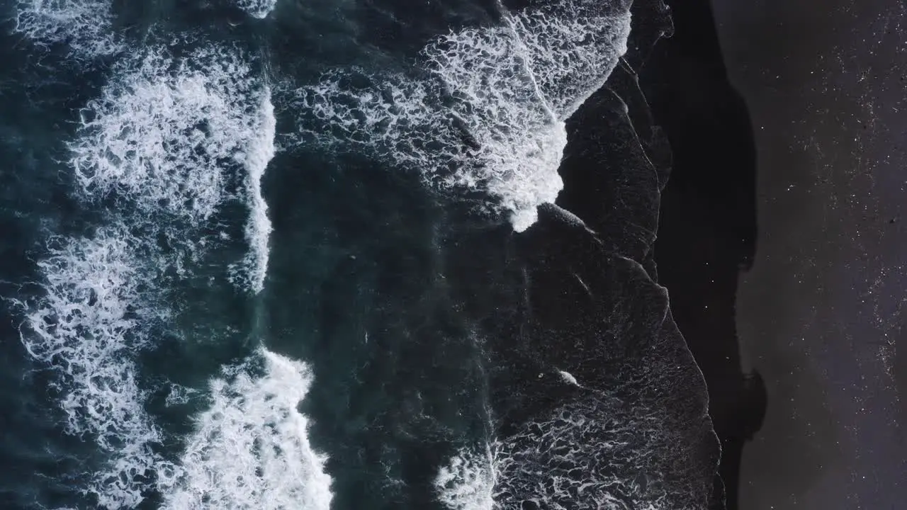 Aerial top down view of water waves reaching the black sand beach in Keramas Bali