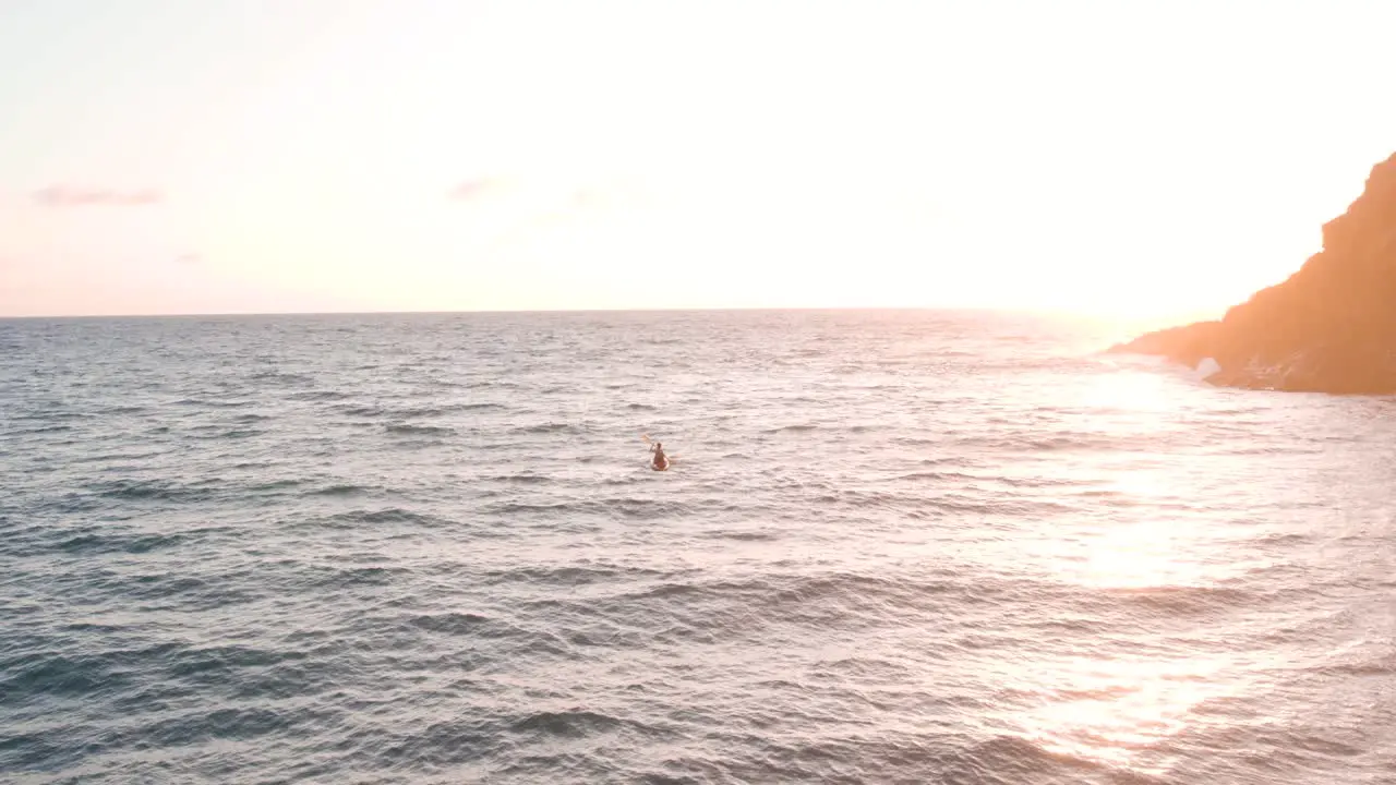 Determined man on kayak paddling against the waves in golden sunrise drone view