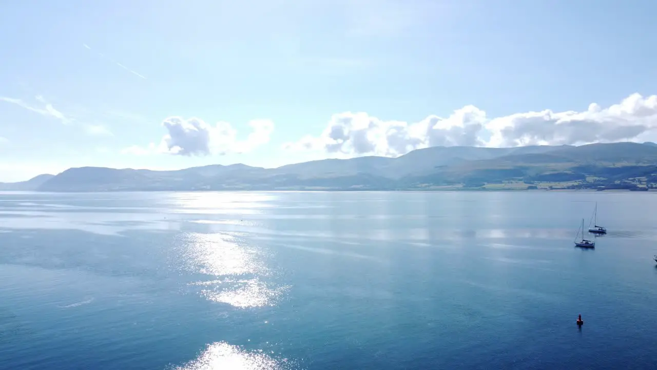 Snowdonia clear mountain range aerial view panning across sunny calm Welsh shimmering seascape