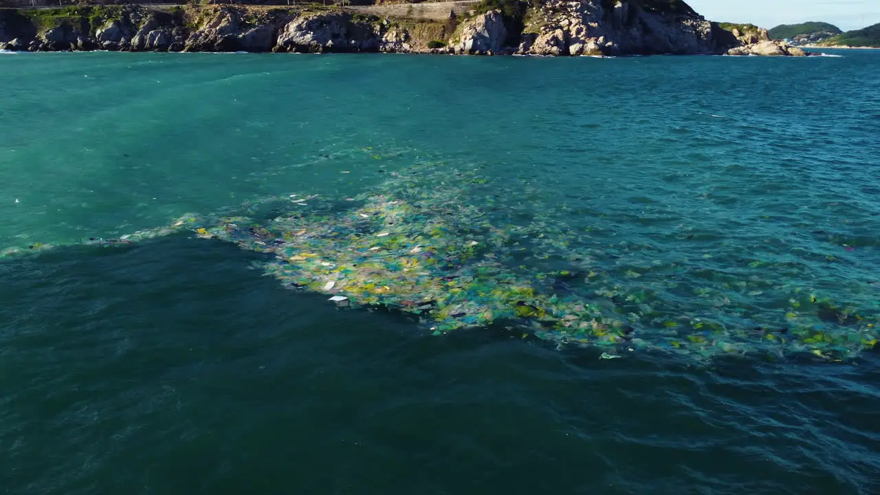 Low aerial circling Vietnamese coast with garbage floating in sea