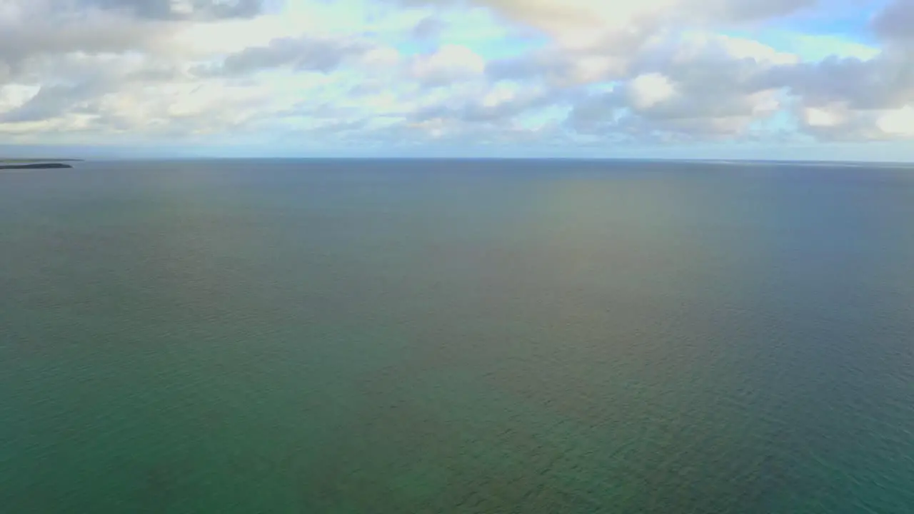 Fly over the ocean while the camera is tilting up to reveal the horizon during a cloudy day