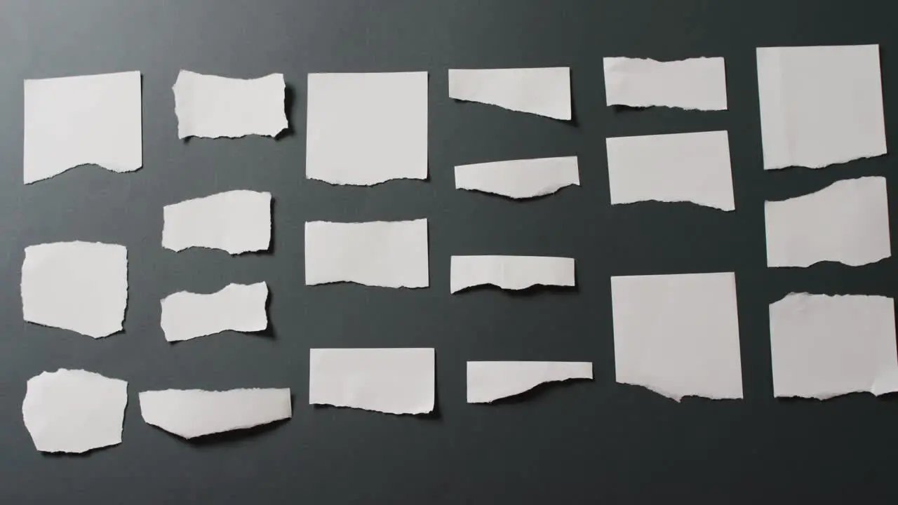 Video of close up of multiple torn piece of white paper with copy space on black background