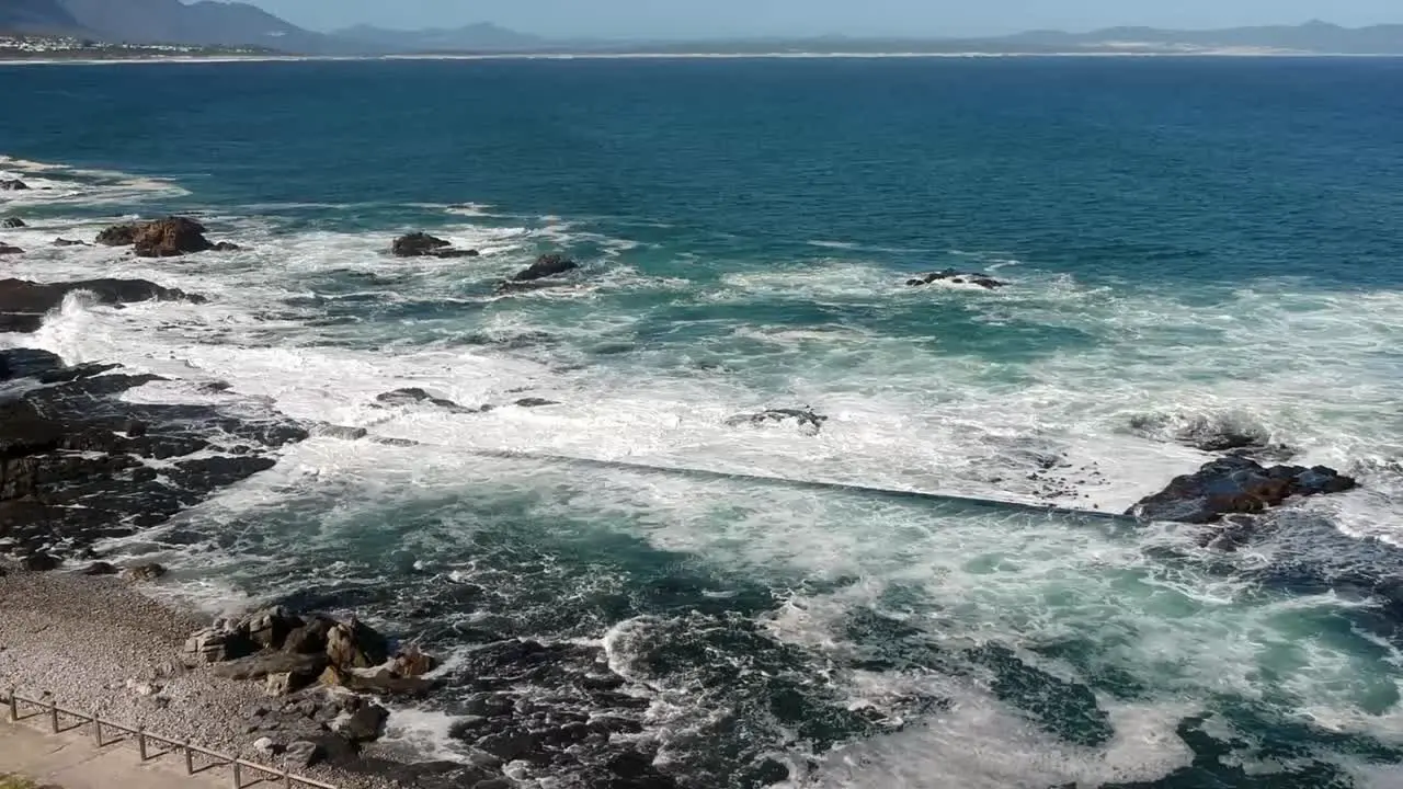 Angled drone view of tidal pool and rocky coastline with waves crashing