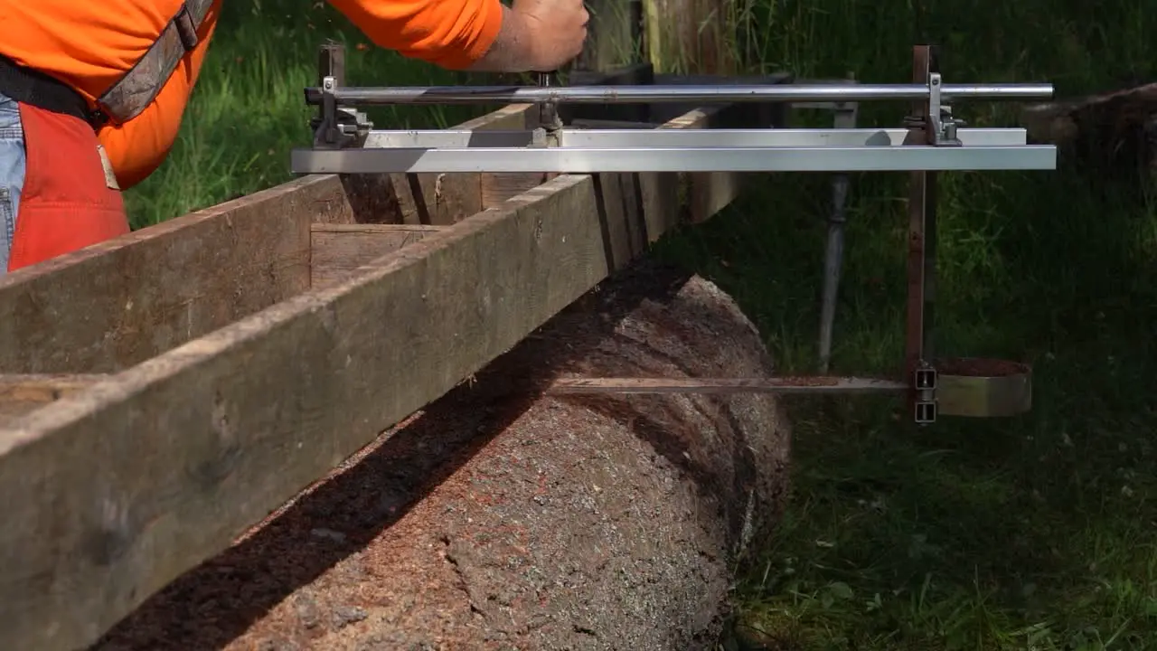 Rear facing medium shot of logger wearing orange using alaskan chainsaw mill on pine log in slow motion