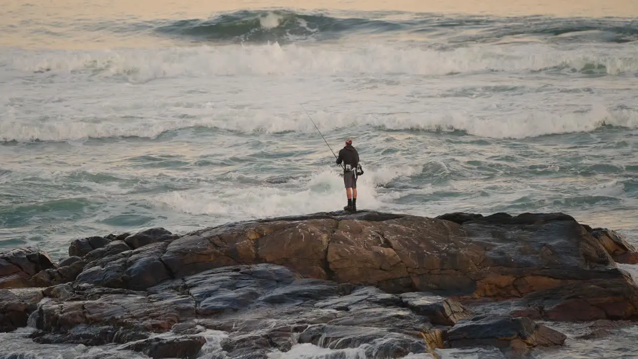 Fisherman saltwater fishing from rocks with waves crashing nearby