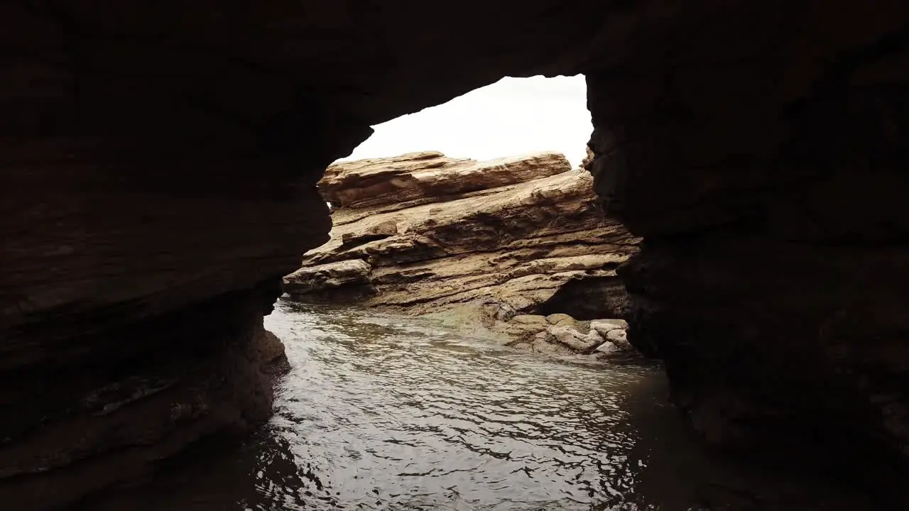 Drone aerial zoom out from a small rocky arch way to reveal ocean and beach