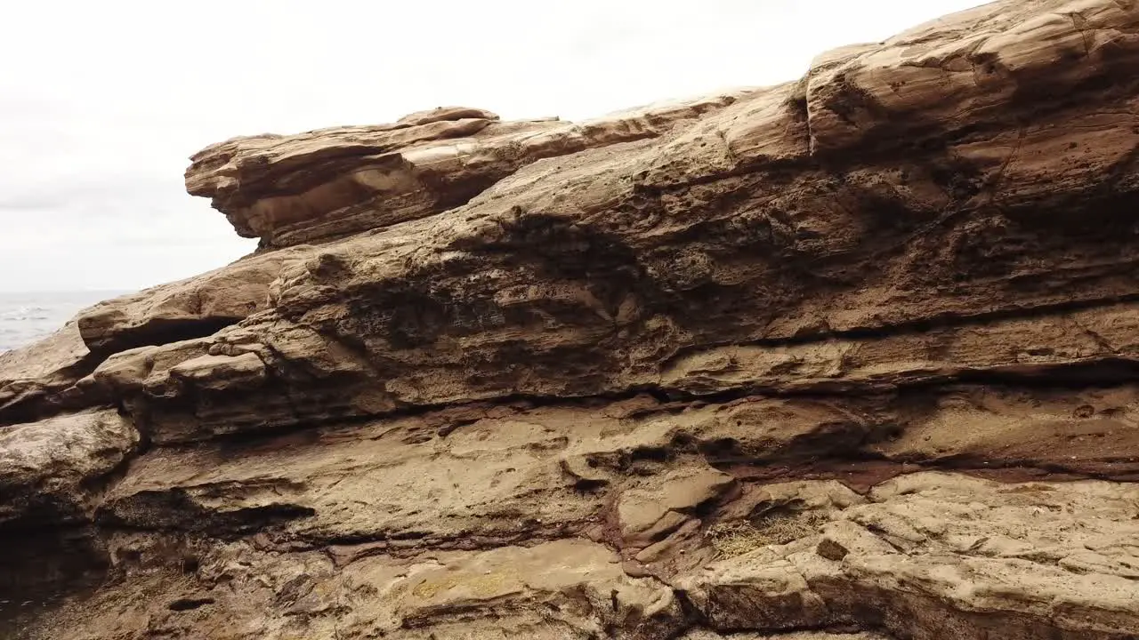 Drone aerial flying through an arch way towards a rocky surface near the ocean