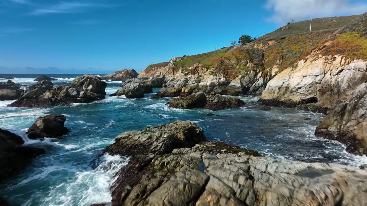 Sweeping view over Blur waves with white caps crashing on brown rocks along pacific coast Highway 1 California