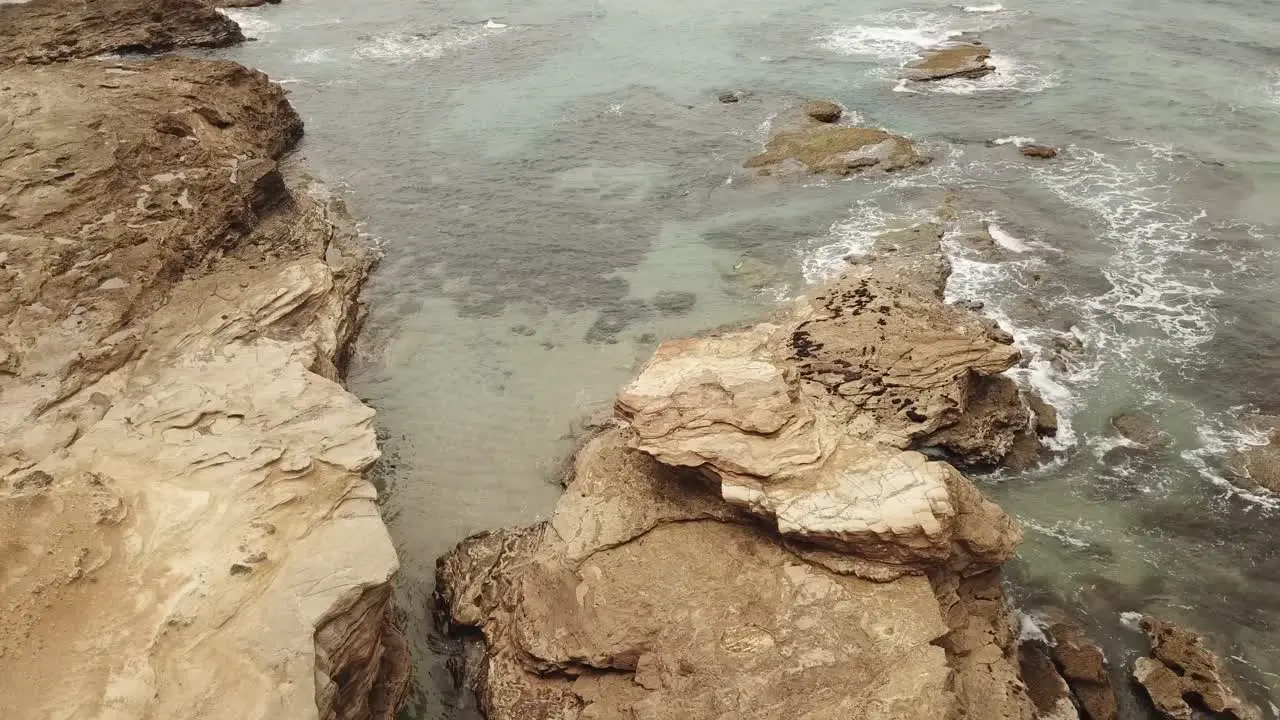 Drone aerial rise and pan down to a rocky landscape with waves crashing onto the face