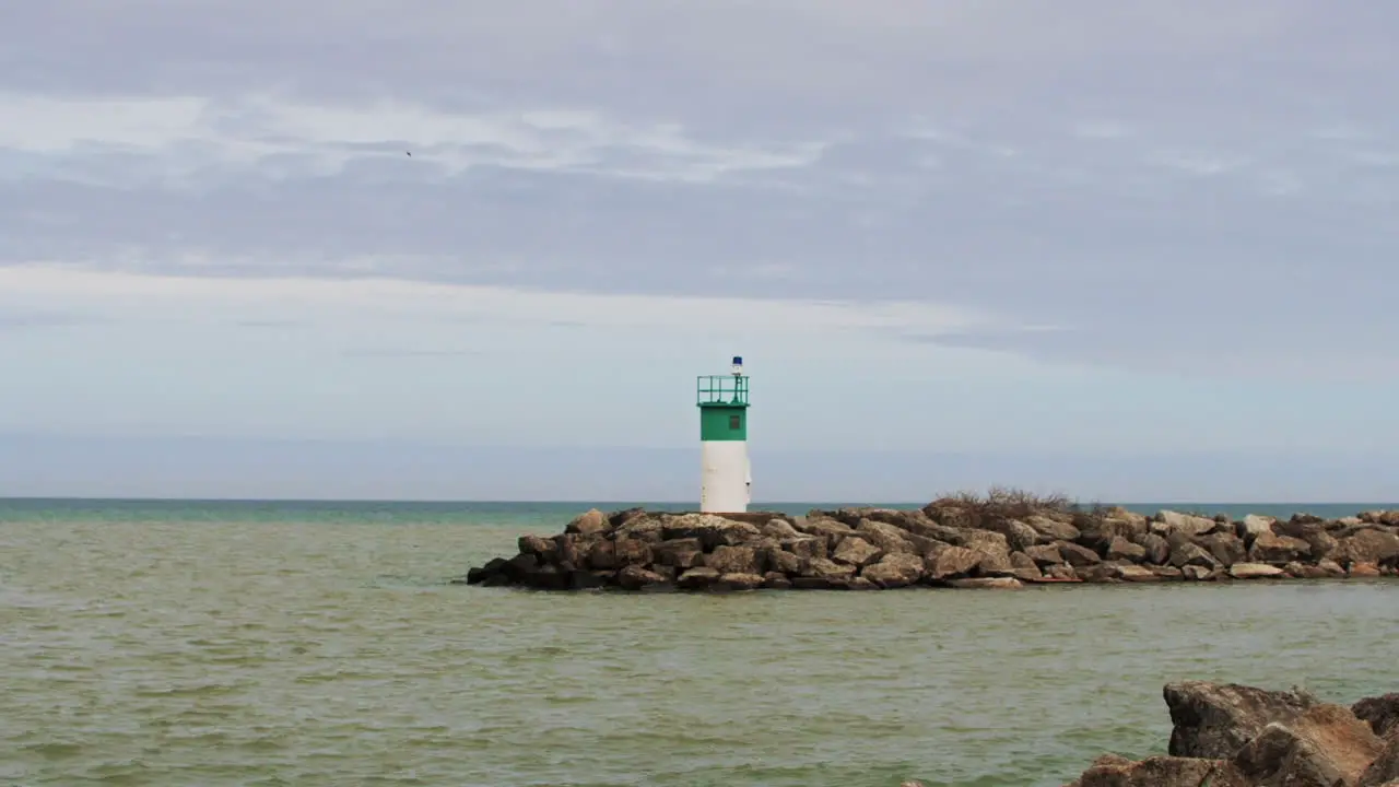 Water moving in slow motion by small green and white lighthouse