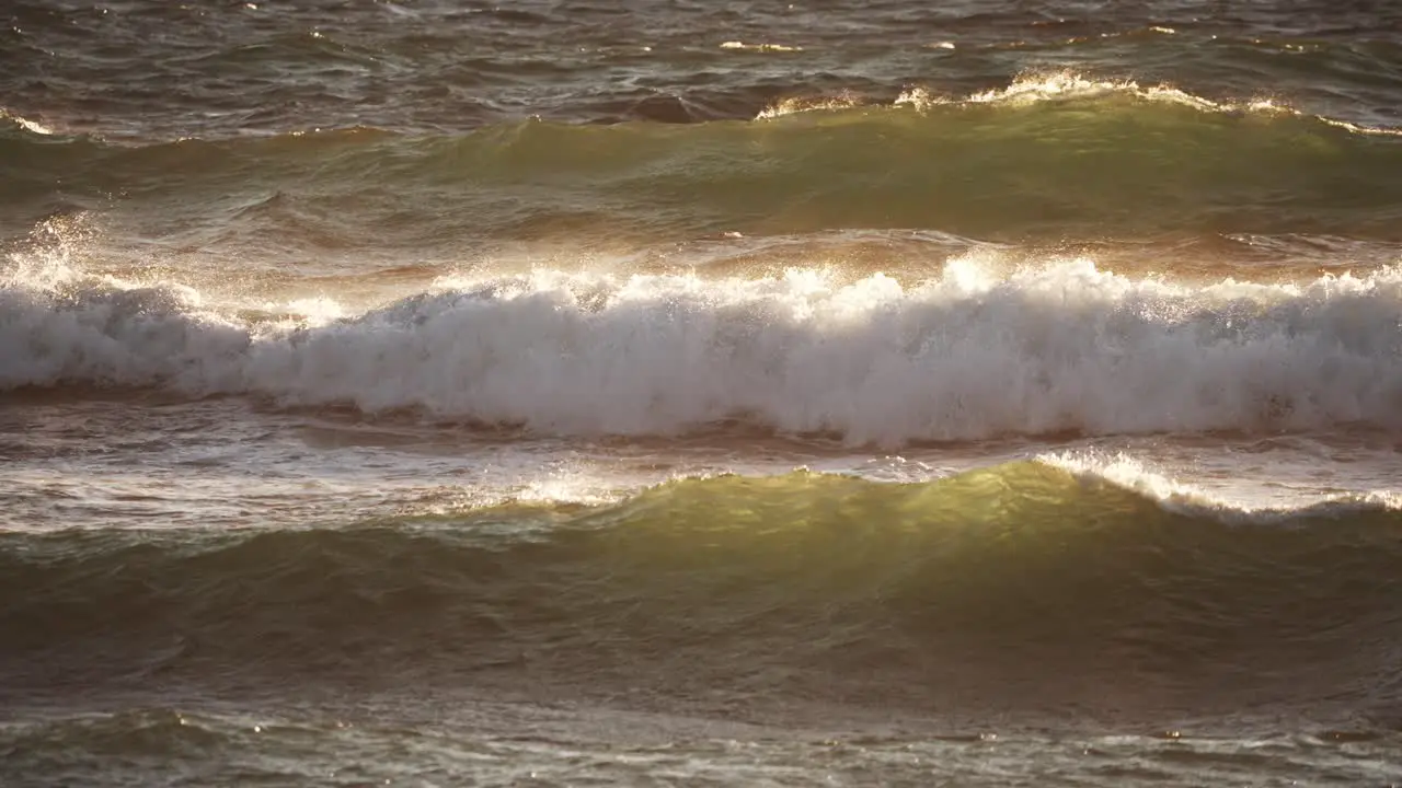 Static shot of waves breaking with a warm glow of the setting sun slow motion