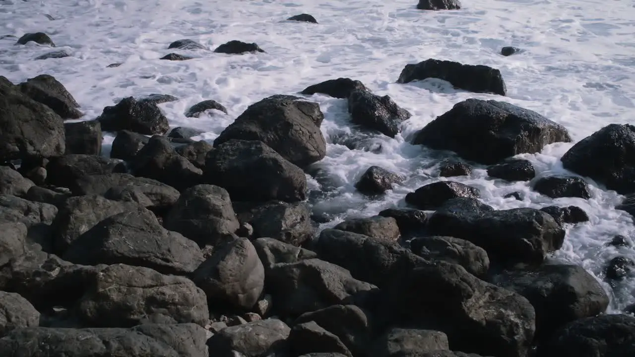 The rocks on the coastline get submerged by a wave