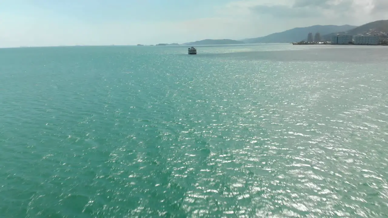 Fly towards a boat in green oceans with beautiful mountains in the background