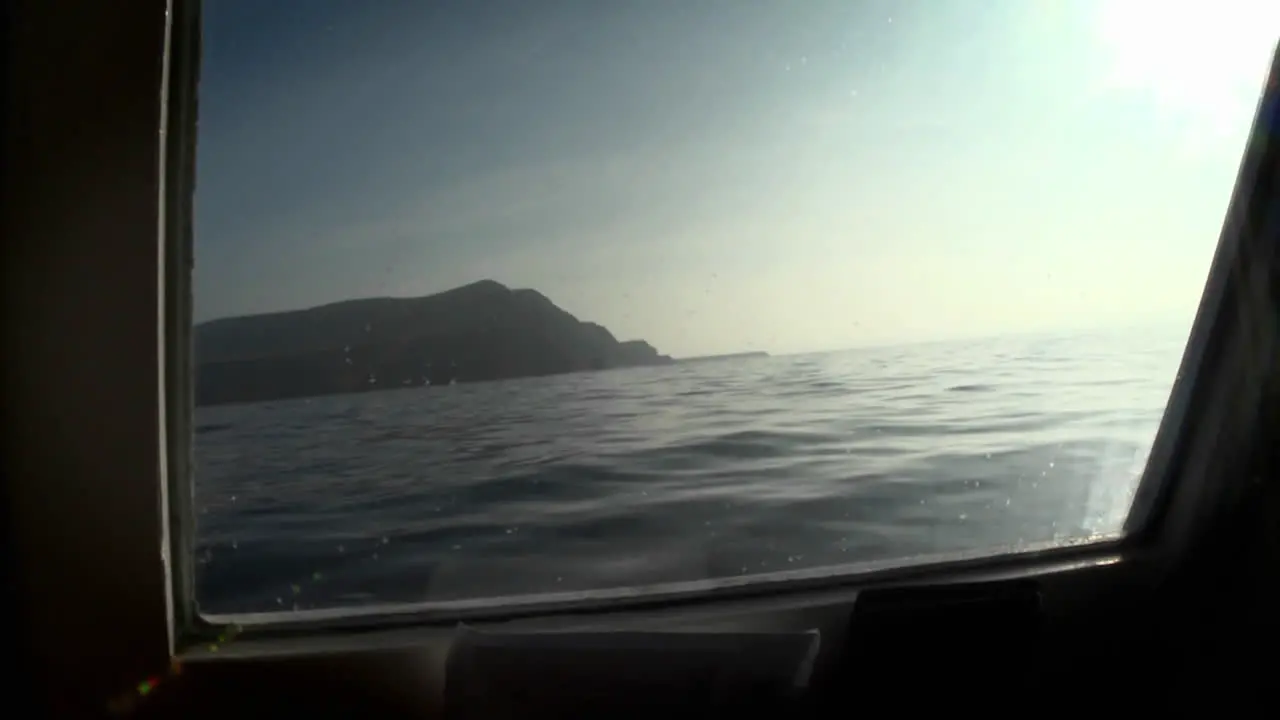 An island is viewed through the porthole of a boat