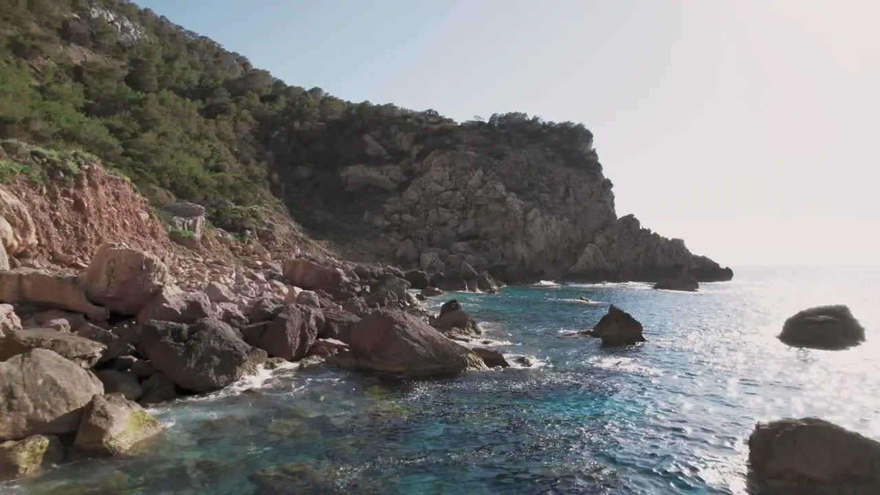 Drone shot coast of Ibiza with rocky cliffs and clear blue ocean water