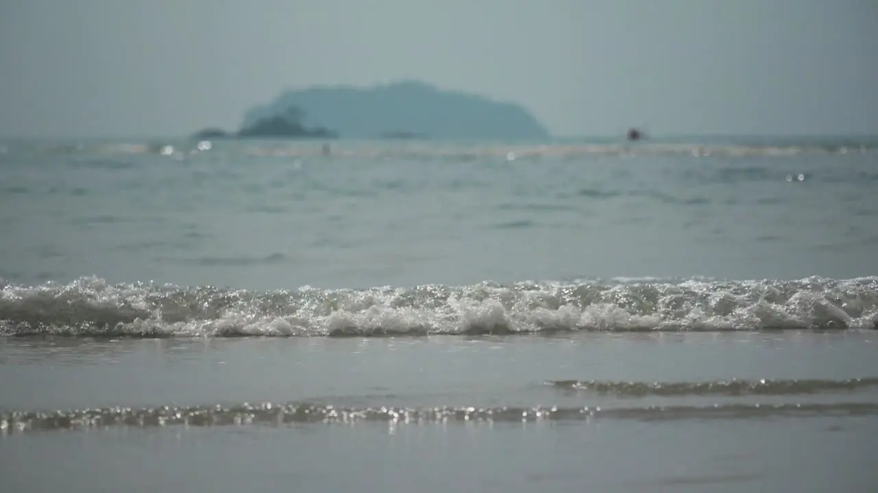 SLOW MOTION Small Ocean Waves Roll In With Hazy Mountain In The Distance