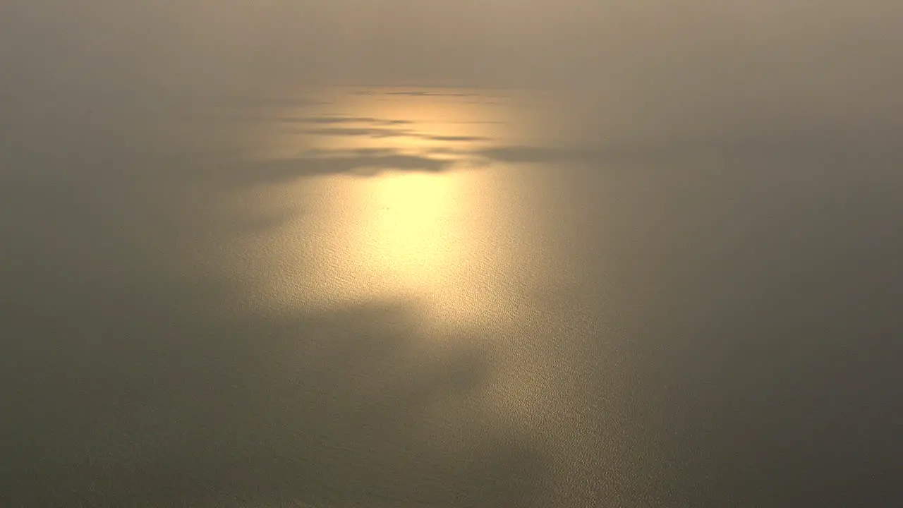 setting sun reflects on the sea with some shadow patches casted by the clouds