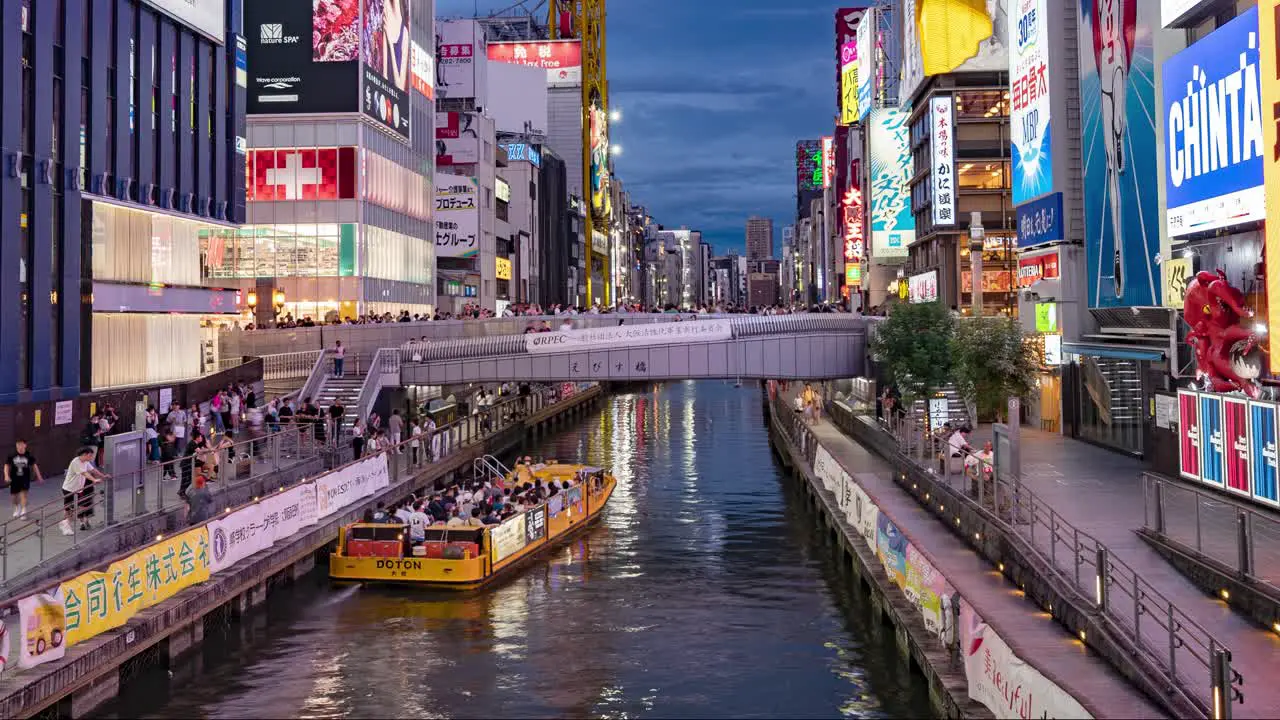 Night Time-Lapse Of Boats passing people and Illuminated signboards at Ebisu Bridge Dotonbori Canal Namba Osaka Japan TILT