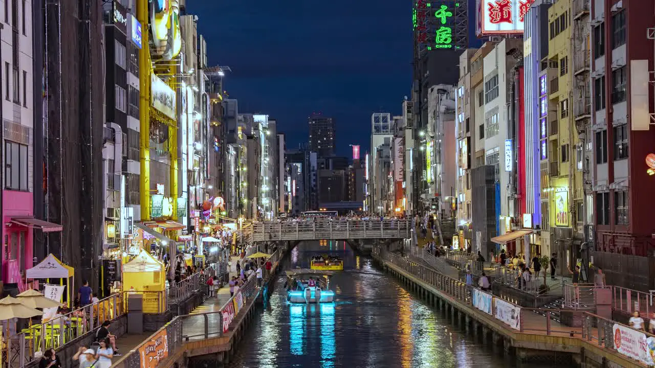 Night Time Lapse Of Boats passing people and Illuminated signboards view from Ebisu Bridge Dotonbori Canal Namba Osaka Japan