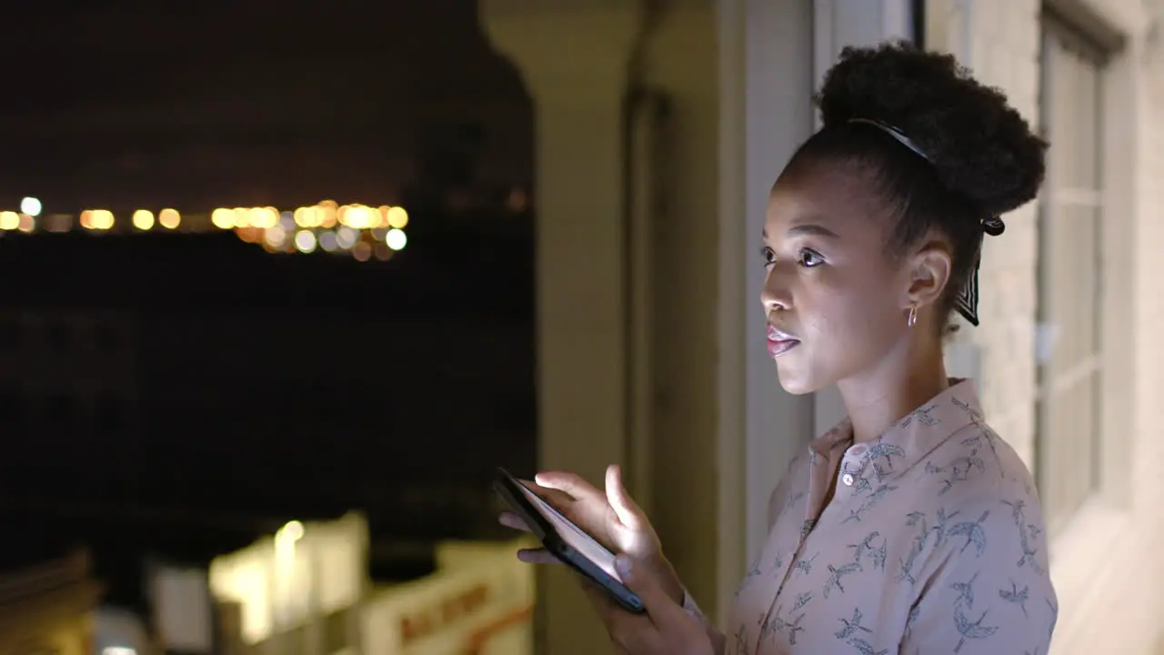 African American woman uses a tablet at night on a balcony with copy space