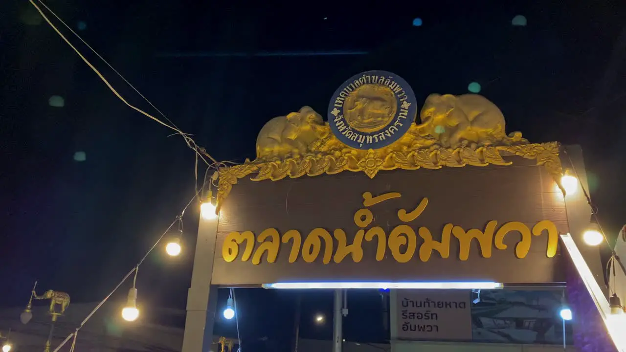 Nighttime view of a Thai temple gate adorned with golden sculptures illuminated by hanging lights