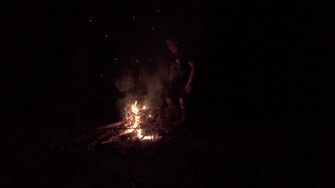  Shot of a man standing and warming himself using fire outdoor during a winter night