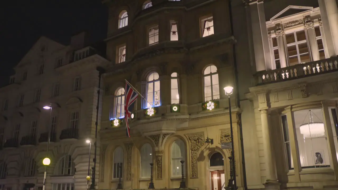 Cinematic shot of architecture of a vintage building with flag of united Kingdom beside a busy road during night in London England